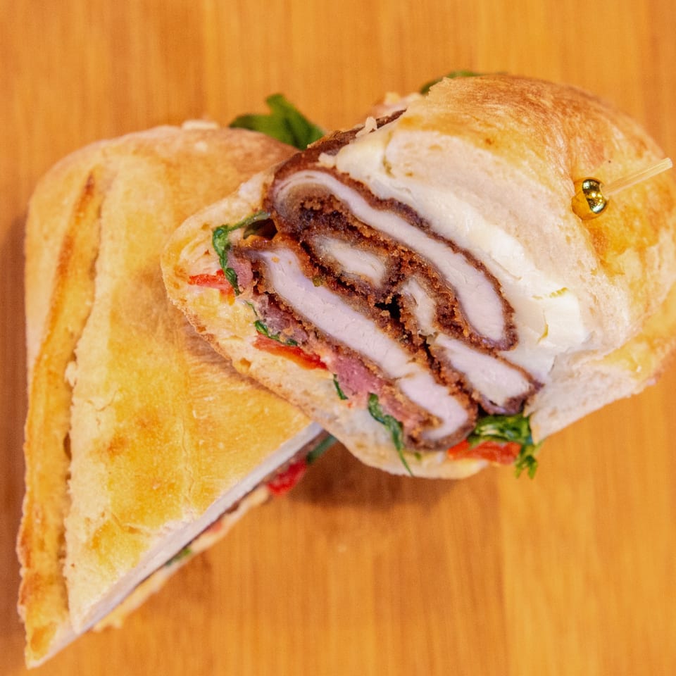 Close-up of a toasted sandwich with layered meat, melted cheese, lettuce, and tomato on a wooden table.