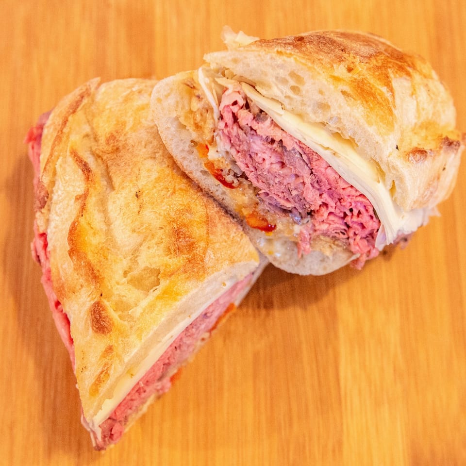 Sliced toasted sandwich filled with pink corned beef, melted cheese, and sauce on a wooden table.