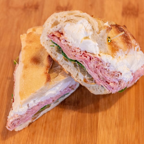 Cross-section of a deli sandwich with pink sliced meat, greens, creamy filling, and crusty bread on a wooden table.